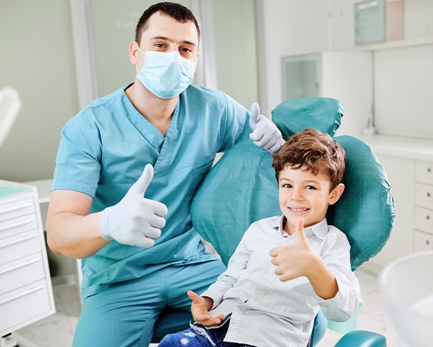 Dentist and young patient giving thumbs up after children's dental checkups and teeth cleanings