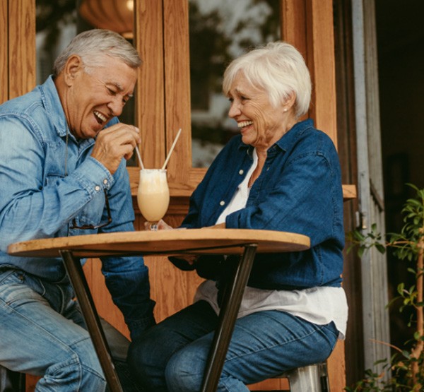 Man and woman with full flawless smiles after tooth replacement with dental implants