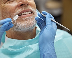 Dentist with blue gloves examining smiling patient's teeth