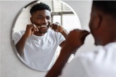 Smiling man flossing teeth in bathroom mirror